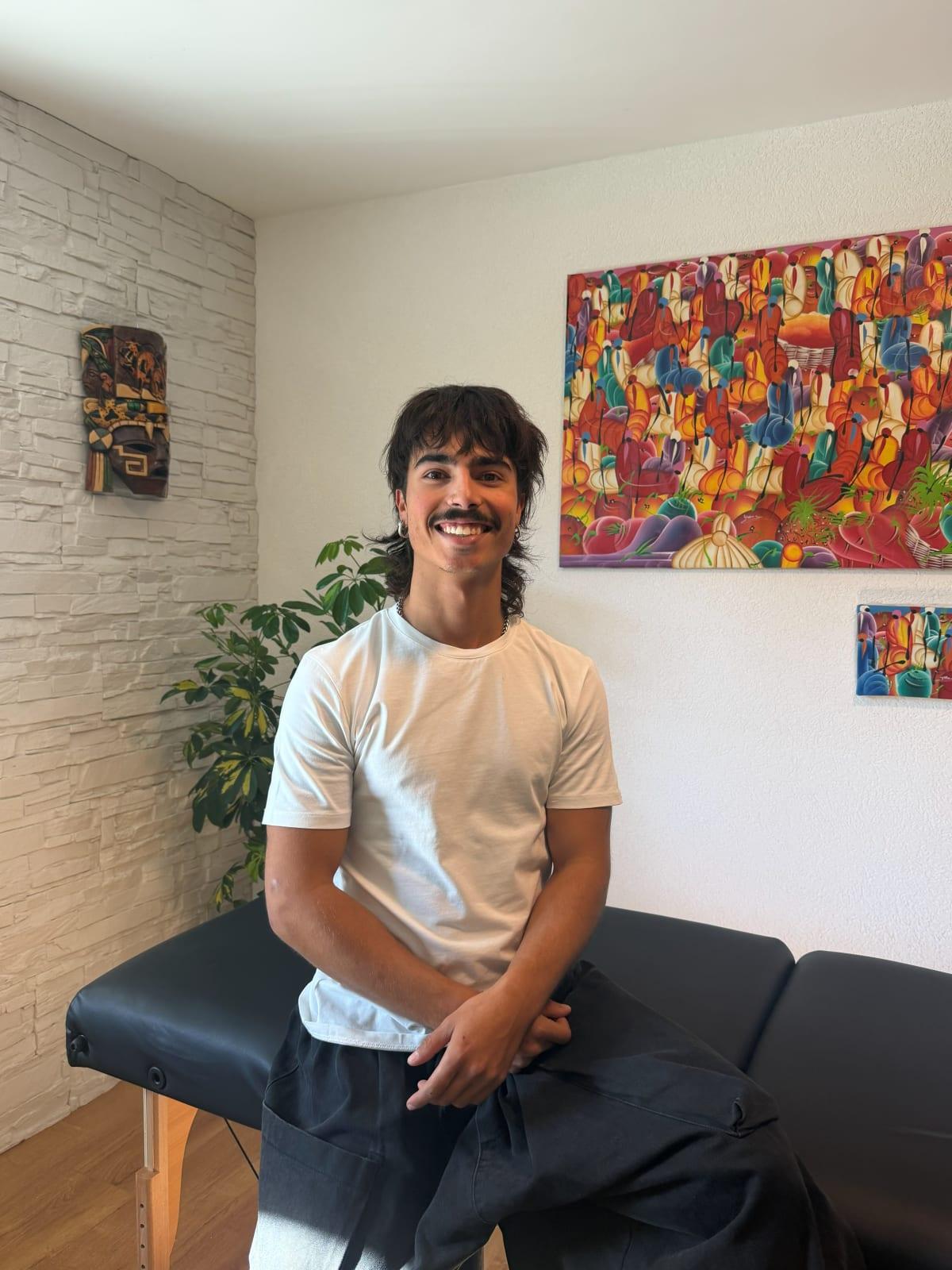 Noah Laface, assis sur sa table de massage, dans son espace.